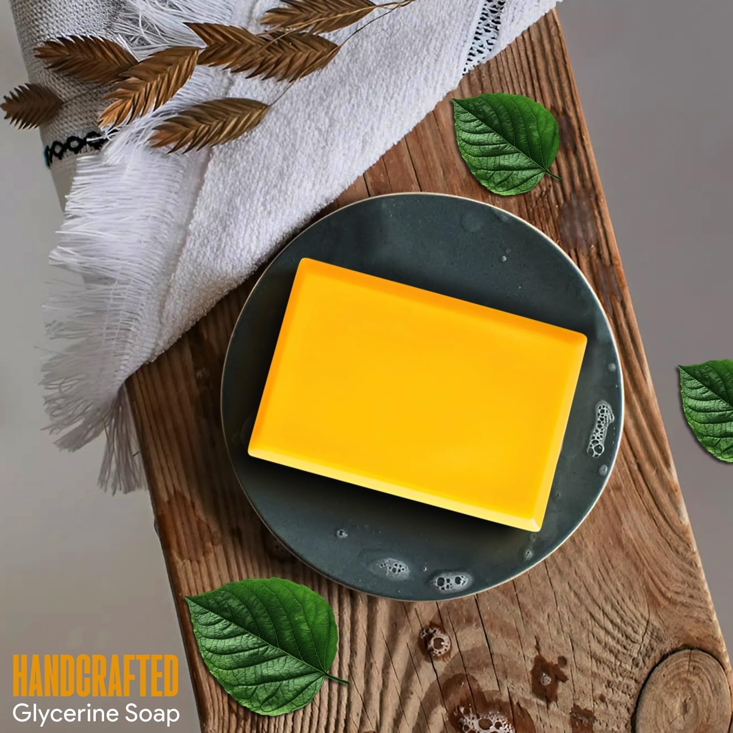 Yellow bar of soap on a dark plate with leaves and a white towel on a wooden surface